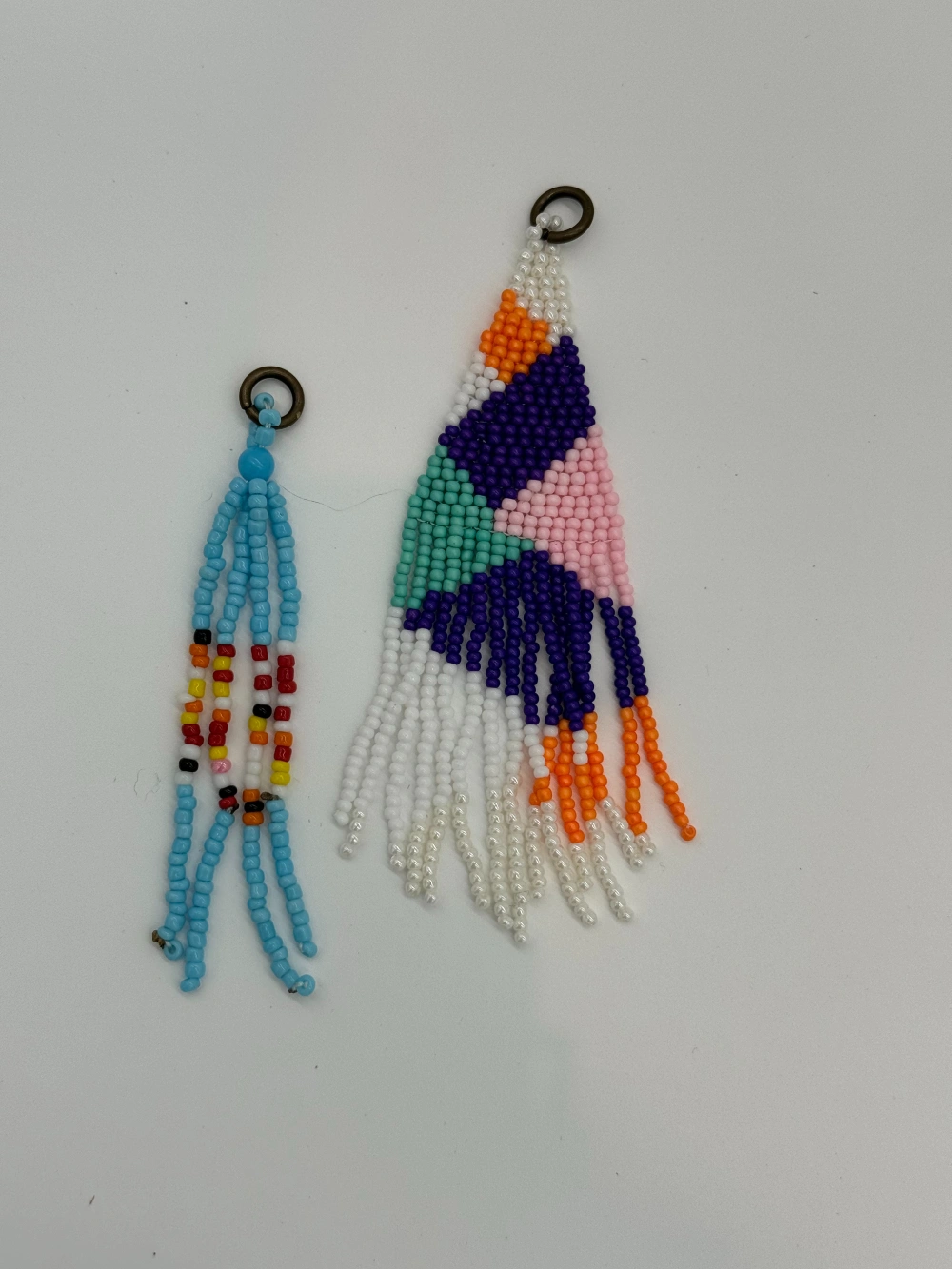 Two beaded earrings are hanging on a wall.