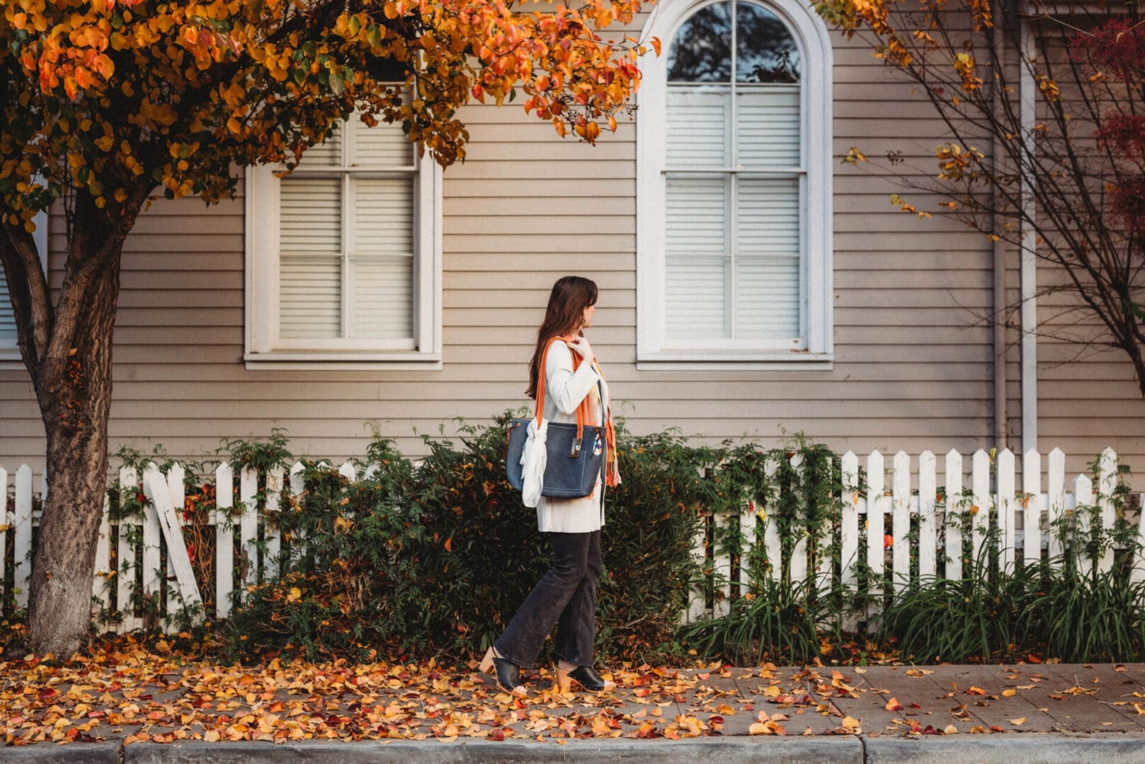 A woman walking down the street in front of a house.