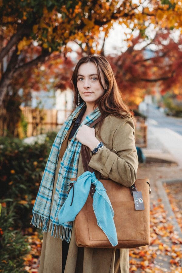 A woman in brown jacket holding blue scarf and purse.