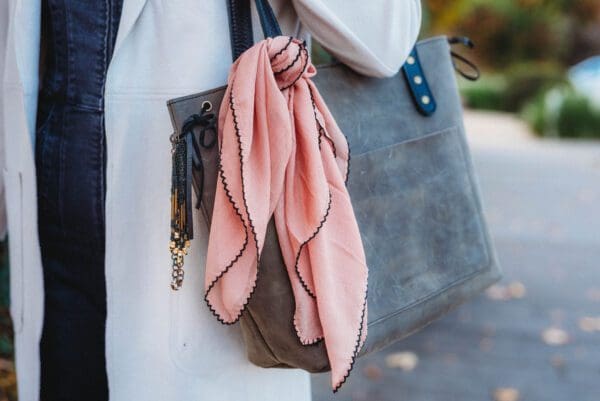 A woman holding onto her purse and wearing a pink scarf