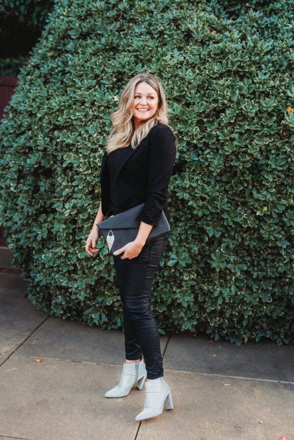 A woman standing in front of a bush holding onto a purse