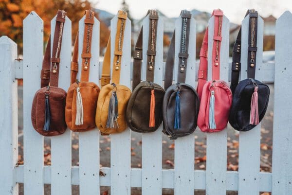 A row of purses hanging on the side of a fence.