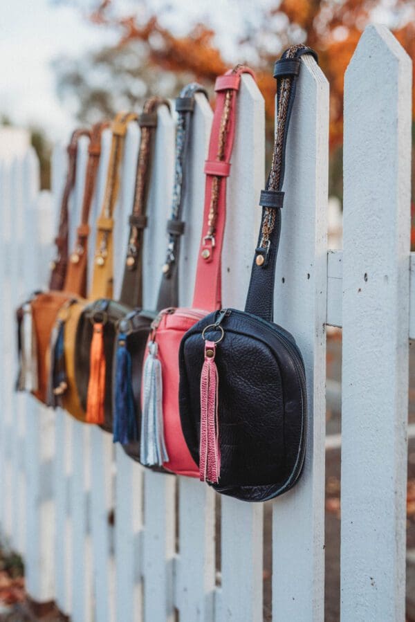 A row of purses hanging on the side of a white fence.