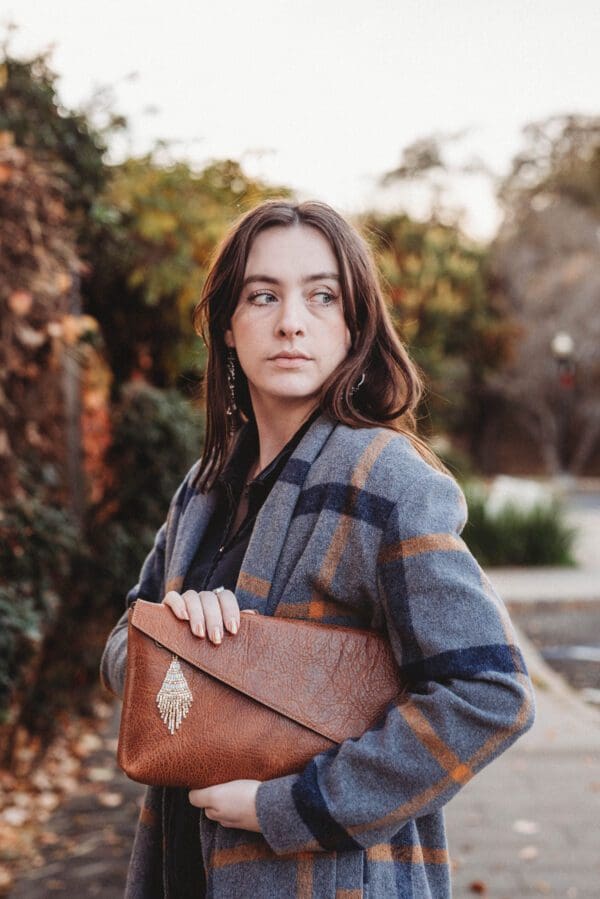 A woman holding onto a brown purse while standing on the street.