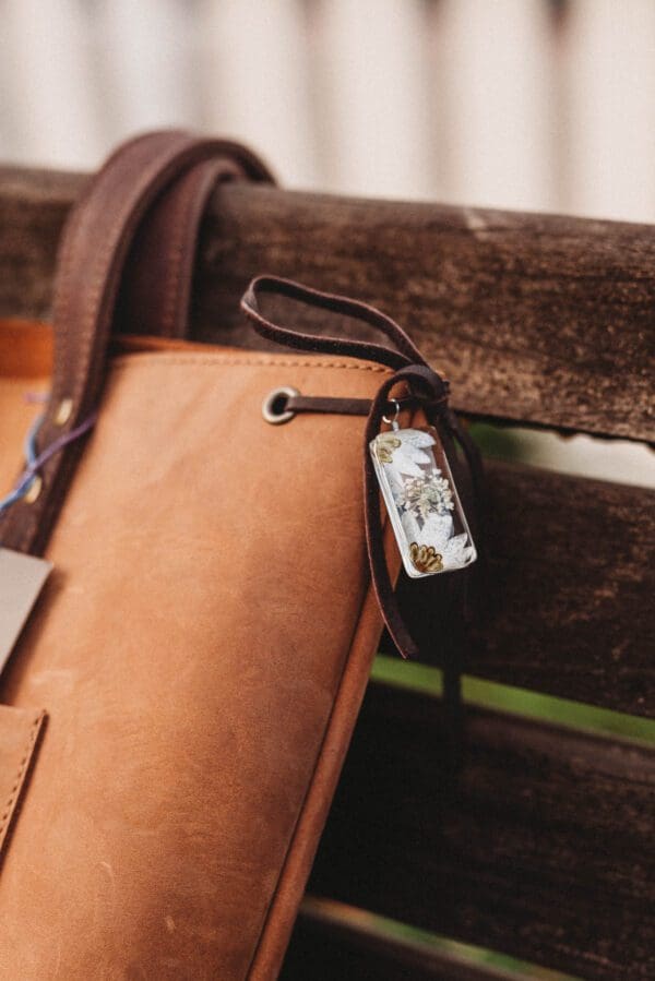 A brown purse with a cell phone hanging from it's strap.