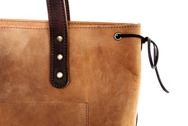 A close up of the handle on a brown leather bag