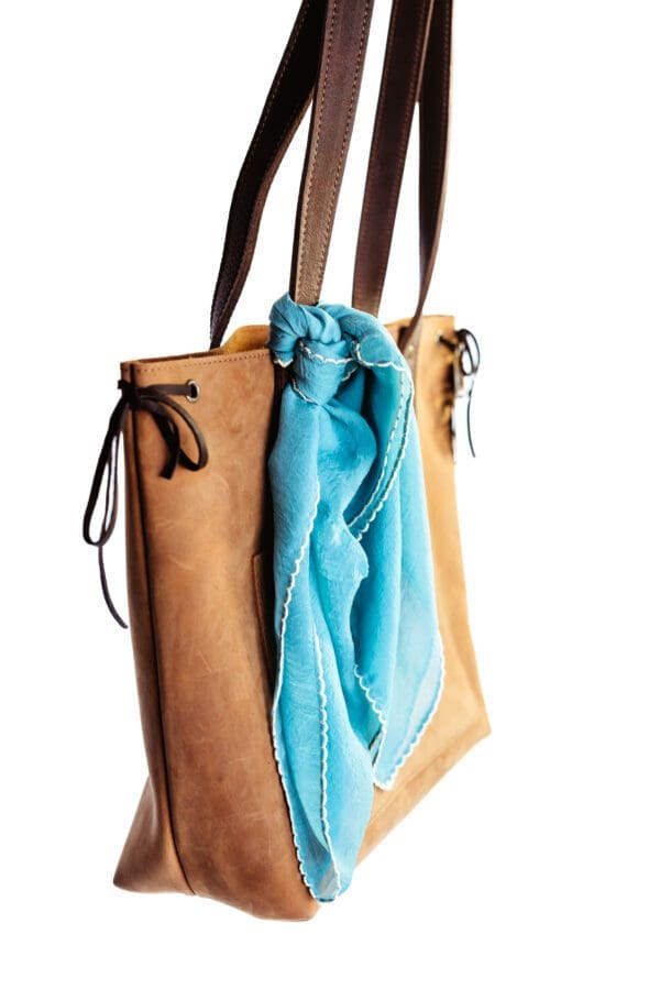 A blue scarf hanging on the side of a brown bag.