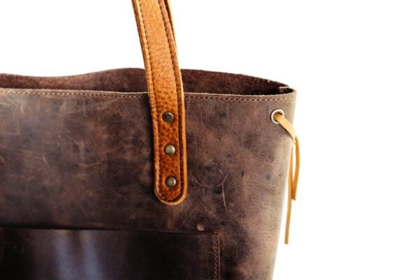 A close up of the handle on a brown leather bag