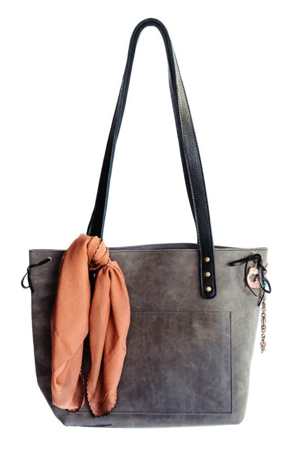 A gray purse with a scarf hanging on the strap.