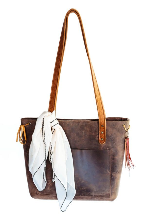 A brown leather bag with a scarf hanging on the side.