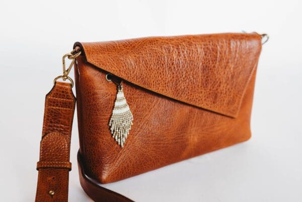 A brown leather purse with a leaf charm on it.