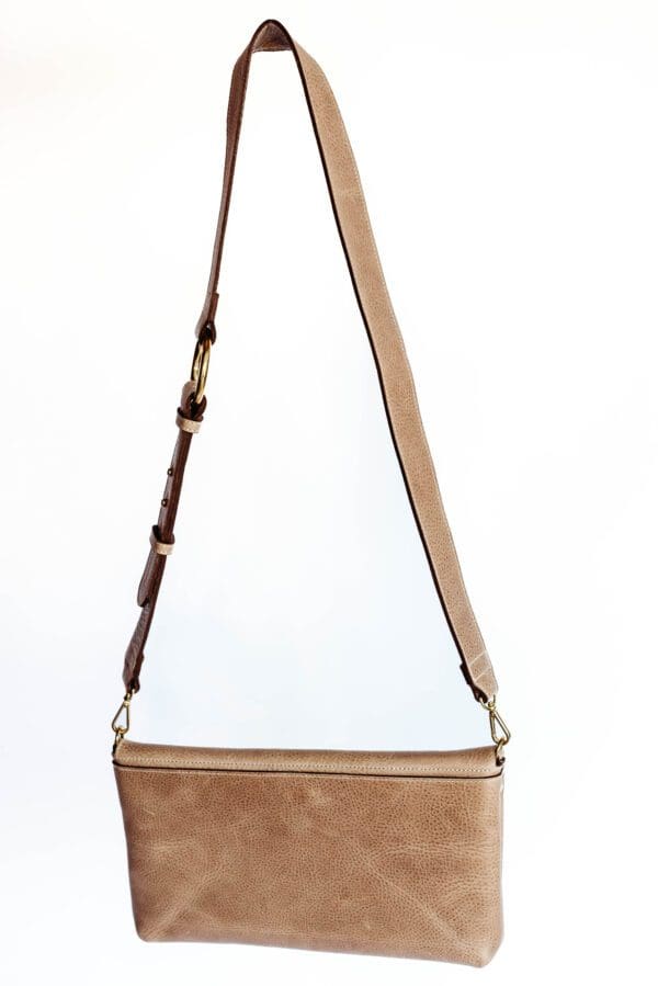 A tan purse is hanging on the wall.