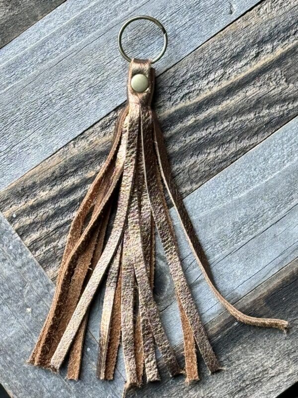 A brown leather tassel keychain with a green bead.