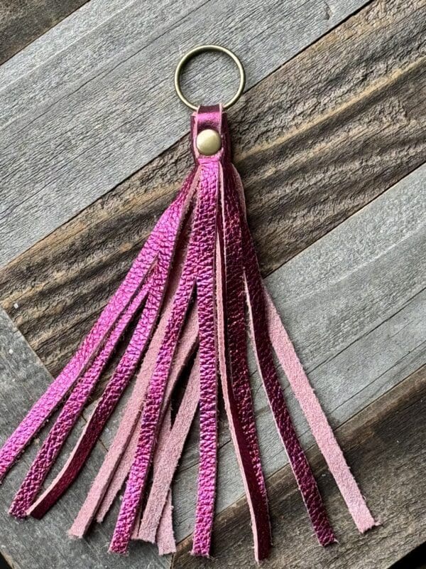 A pink leather keychain with tassels hanging on a wooden table.