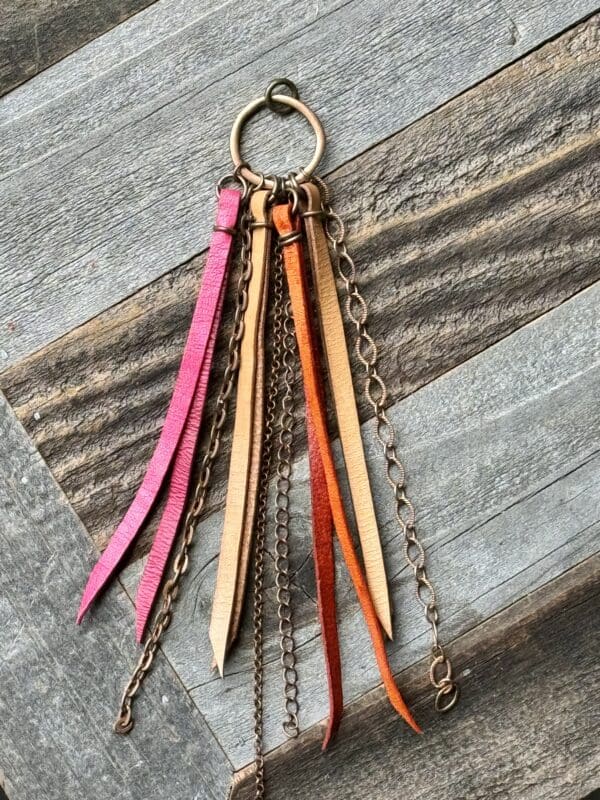 A wooden key chain with leather tassels hanging from it.