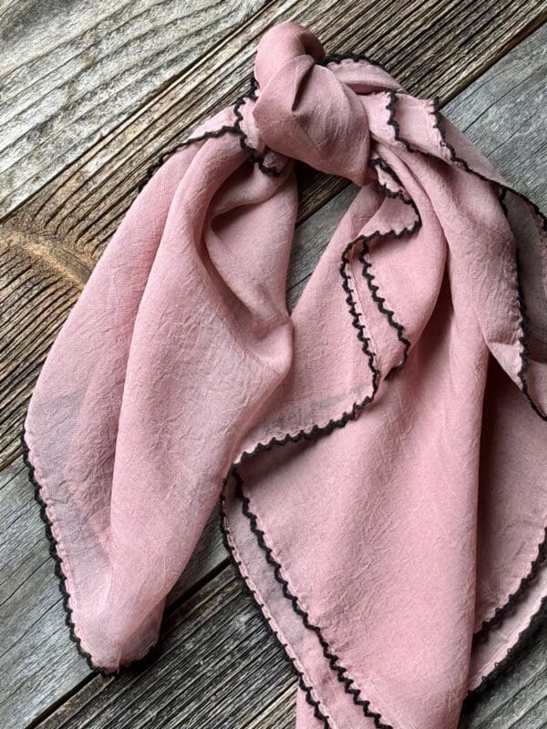 A pink scarf with black trim on top of a wooden table.