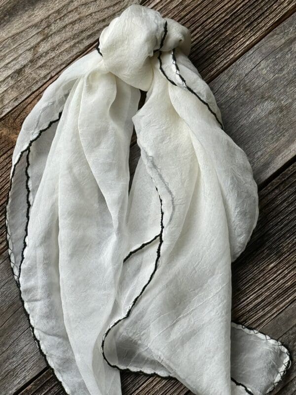 A white scarf with black trim on top of a wooden table.