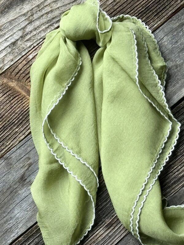 A green scarf with white trim on top of wooden table.