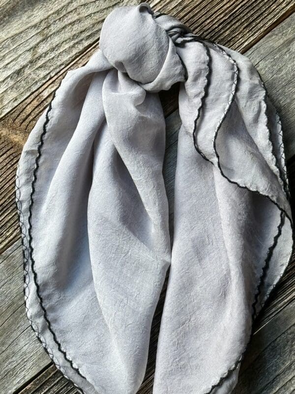 A gray scarf with black trim on top of a wooden table.