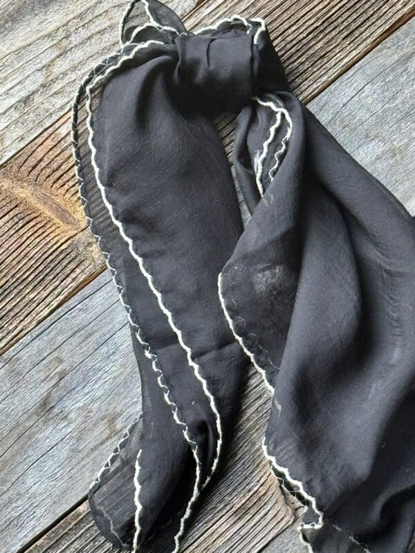 A black scarf with white trim on top of a wooden floor.