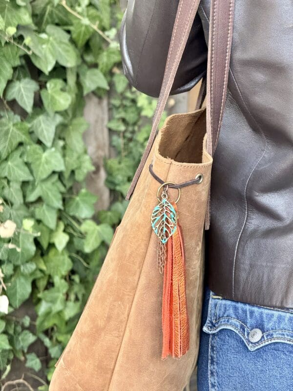 A person holding onto a brown purse with orange tassels.