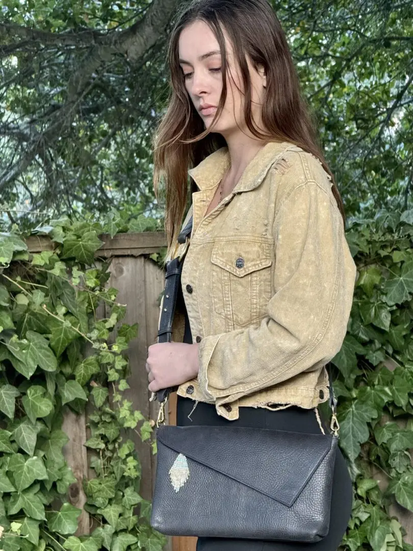 A woman standing in front of some bushes holding onto a purse