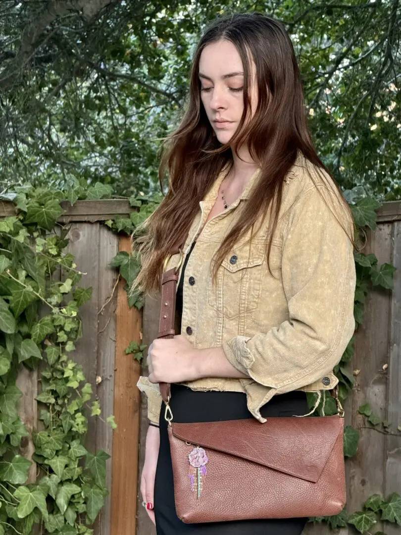 A woman standing in front of a fence holding onto a brown purse.