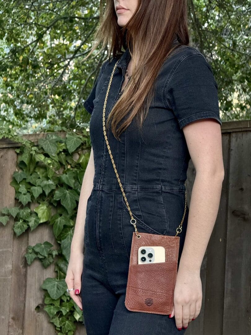 A woman wearing a black jumpsuit and holding a brown purse.