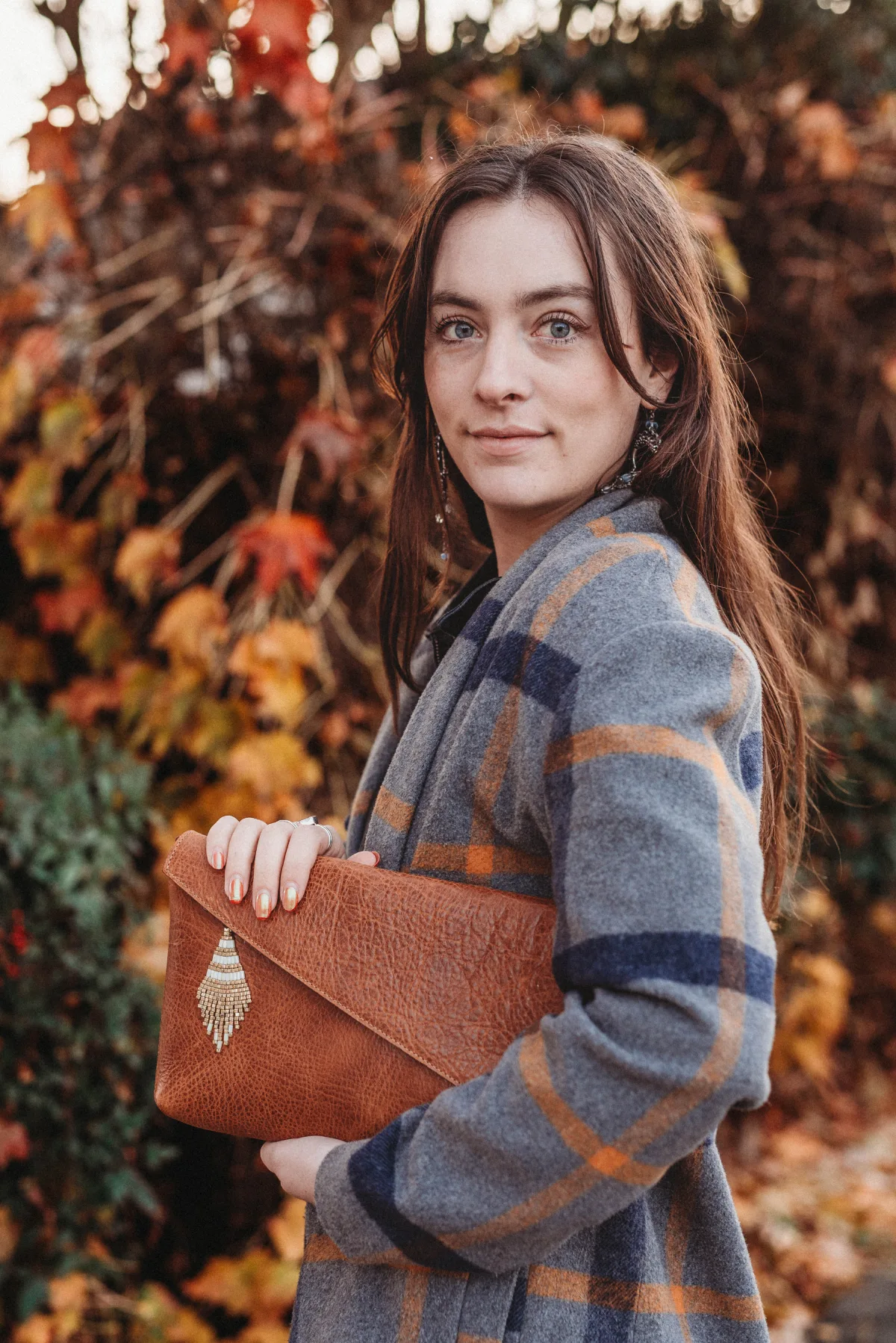 A woman holding onto a brown purse in front of some trees.